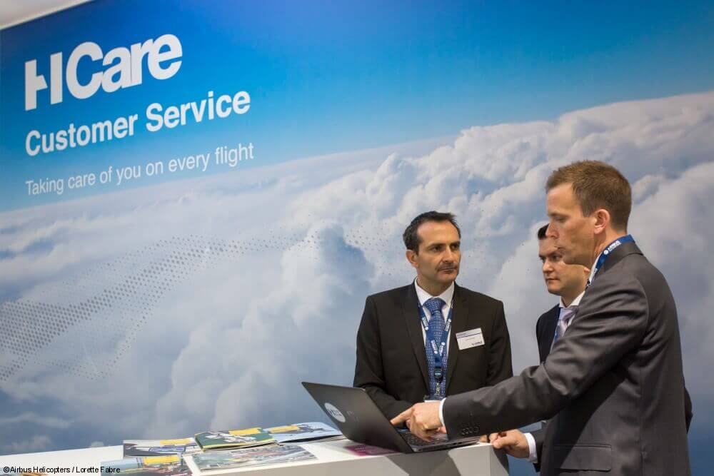 Three men stand next to a computer with HCare logo on wall behind them