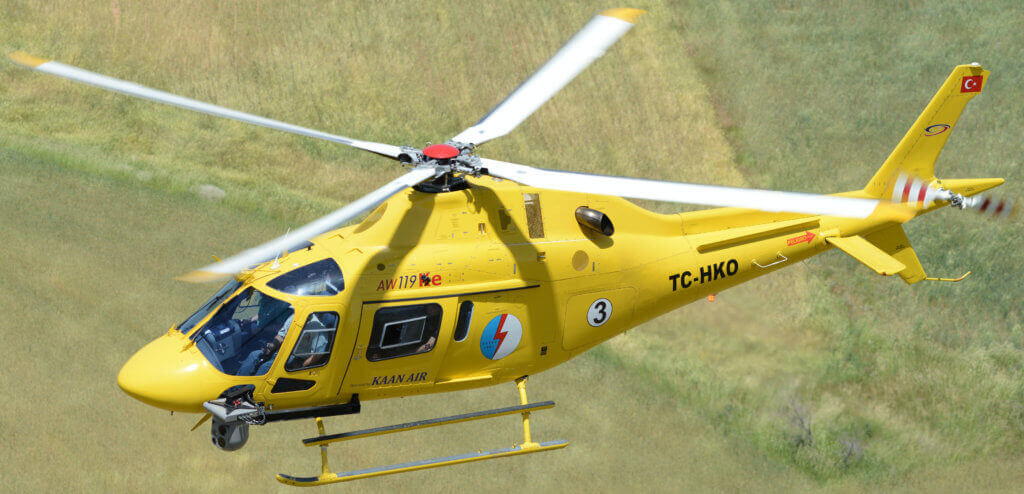 Yellow AW119 helicopter with TrakkaCam mounted on it, in flight.