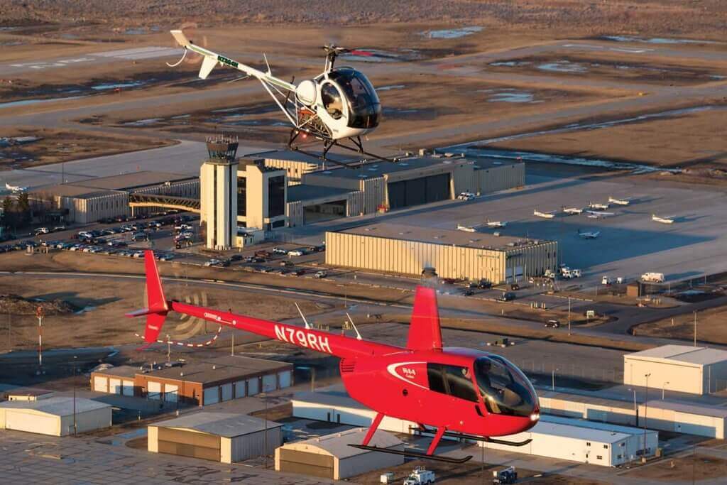 UND operates the S-300 and Robinson R44 in its fleet. Here, the two types fly with the UND aerospace airport campus in the background.
