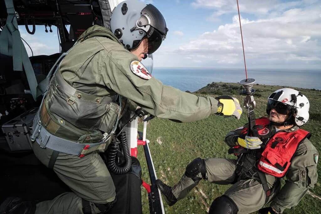 The hoist operator reaches out to grab the rescue swimmer as he is brought back up to the aircraft.