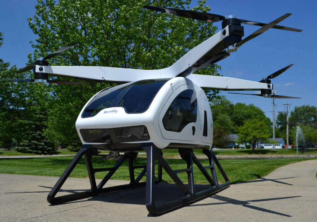 The SureFly features a two-seat cabin that more closely resembles an automobile chassis than a helicopter airframe, with lift provided by eight single-blade propellers  one above and one below each of four foldable arms that reach out in an 