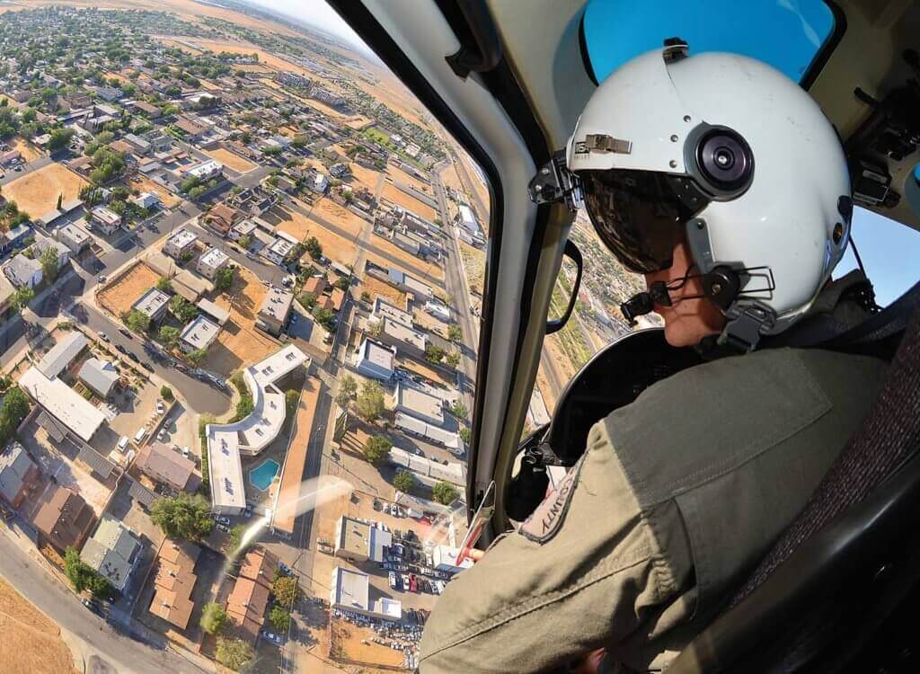 Man in cockpit of helicopter, wearing white helmet.