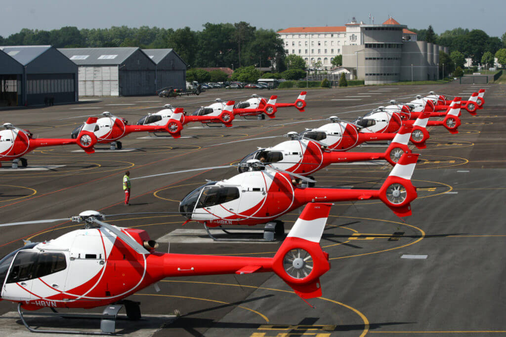Several red and white helicopters rest on ground