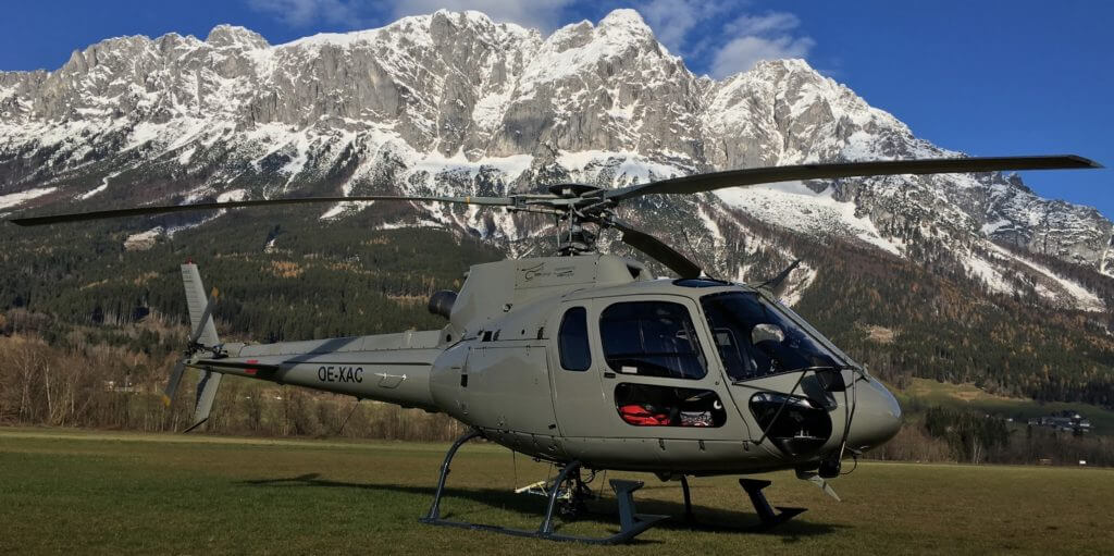 Helicopter rests on ground, with mountains in background.
