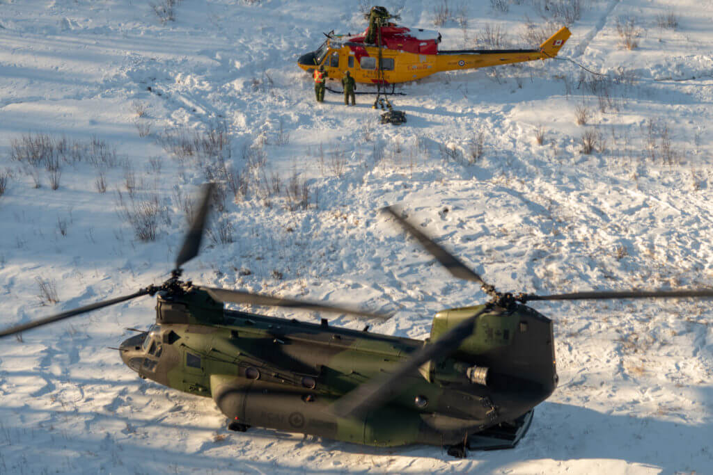 A CH-147F Chinook helicopter rests on the snow in the Cold Lake Air Weapons Range near a damaged CH-146 Griffon helicopter. Slings are being attached to the Griffon, which has had equipment such as its blades and tail rotor removed in preparation for the Chinook airlifting it back to 4 Wing. MCpl Amy Martin Photo